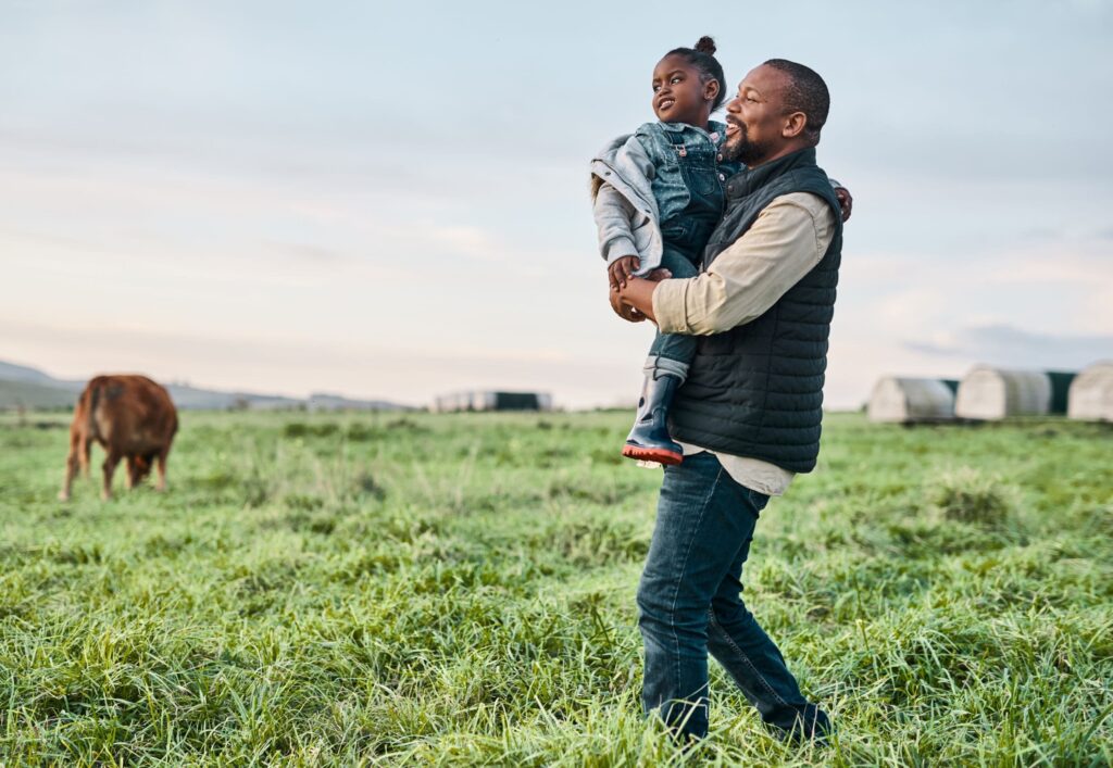 father carrying his young daughter through a cow pasture