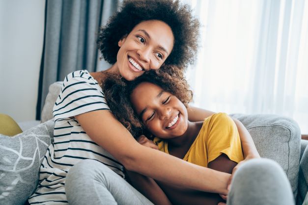 Mother and daughter cuddling on the couch and smiling.