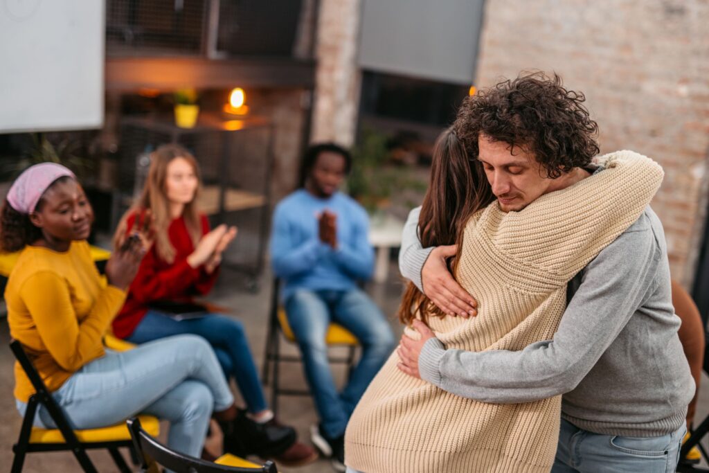People at a group meeting; two people hugging