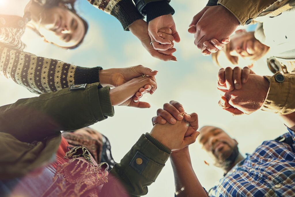 Looking up to a group of adults standing in a circle holding hands. Blue sky is in the background.